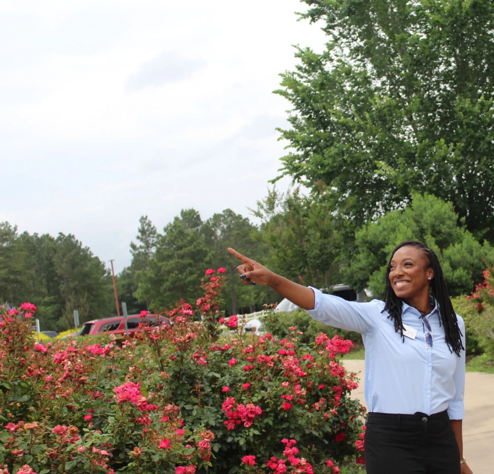 Nicole King smiling and pointing while standing among flowering bushes.